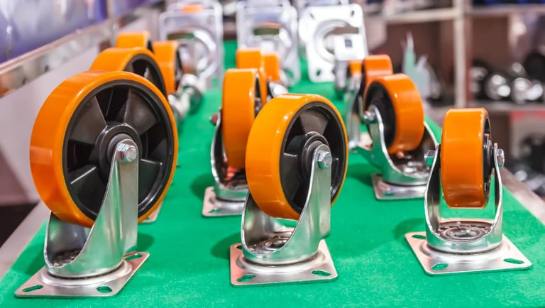 Collection of industrial caster wheels with orange rubber treads and chrome metal bases mounted on a green surface