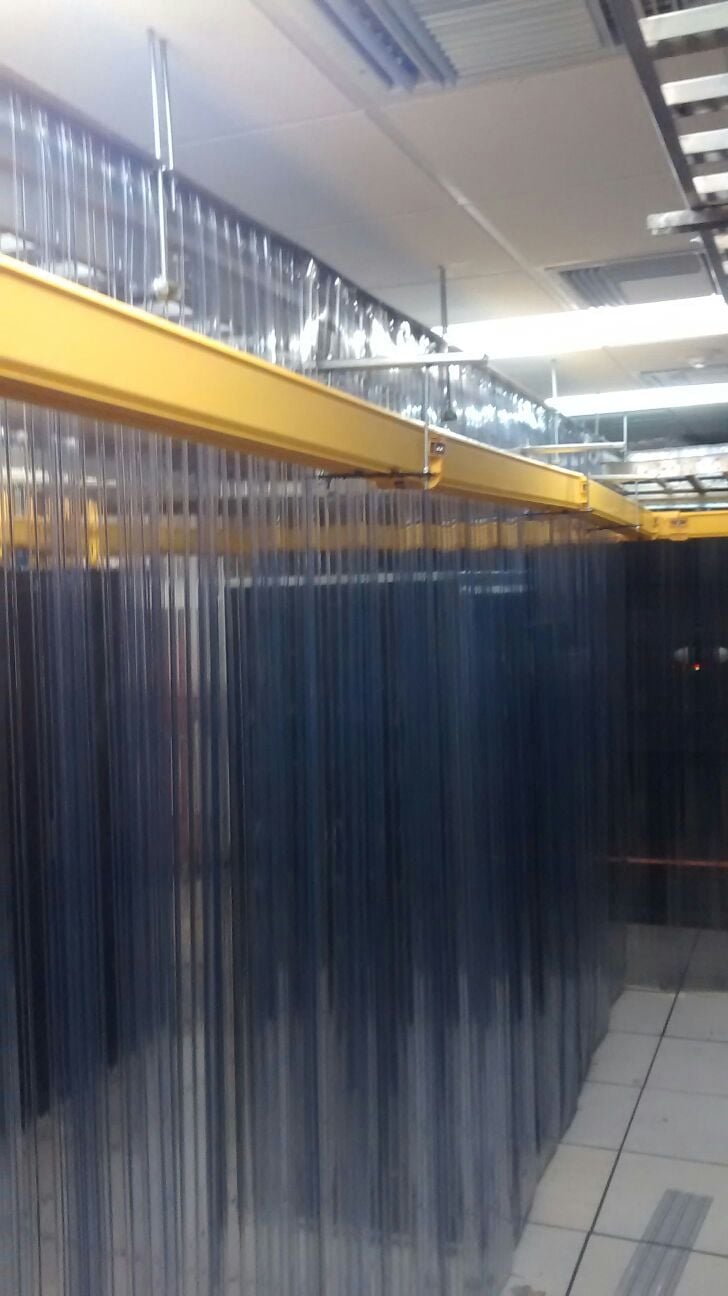 Industrial warehouse interior with yellow overhead crane beam and blue corrugated metal storage enclosure under fluorescent lighting